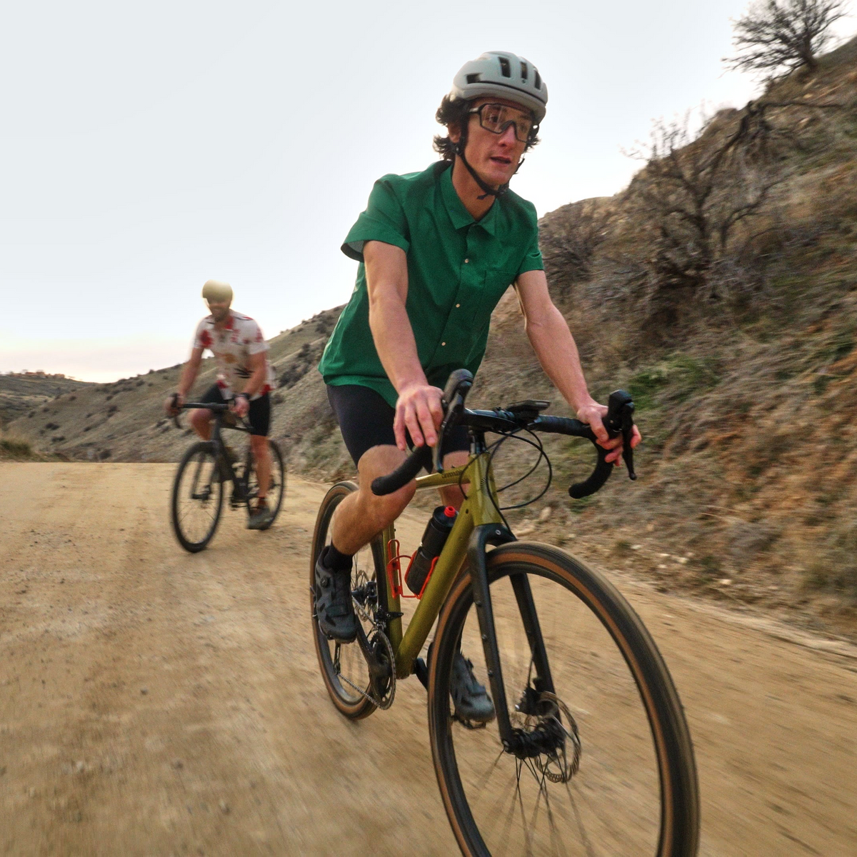 Two cyclists riding on a dirt road with a mountainous landscape.