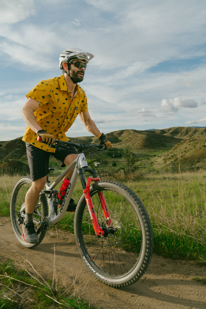 smiling mountain bike rider wearing a rowdee snap shirt in the trails and tacos yellow colorway